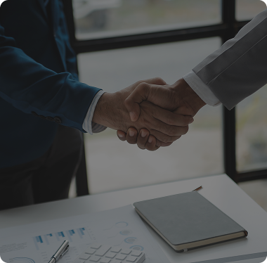 Close-up of two business partners shaking hands over a desk with a notebook and pen, representing PRG MFT's core values of trust and partnership