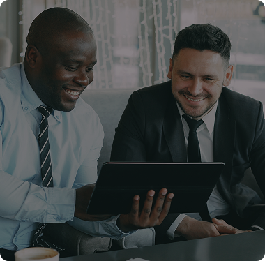 Two smiling business professionals in suits reviewing an investment plan on a tablet together, representing PRG MFT's vision